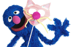 Grover, a character from Shalom Sesame, holding a mask for Purim, one kind of costume worn on the Jewish holiday